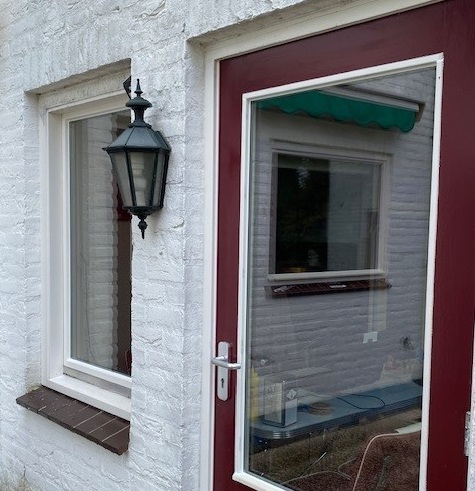 Wit geschilderde gevel met een donkerrode voordeur en raamkozijn met nieuwe beglazing