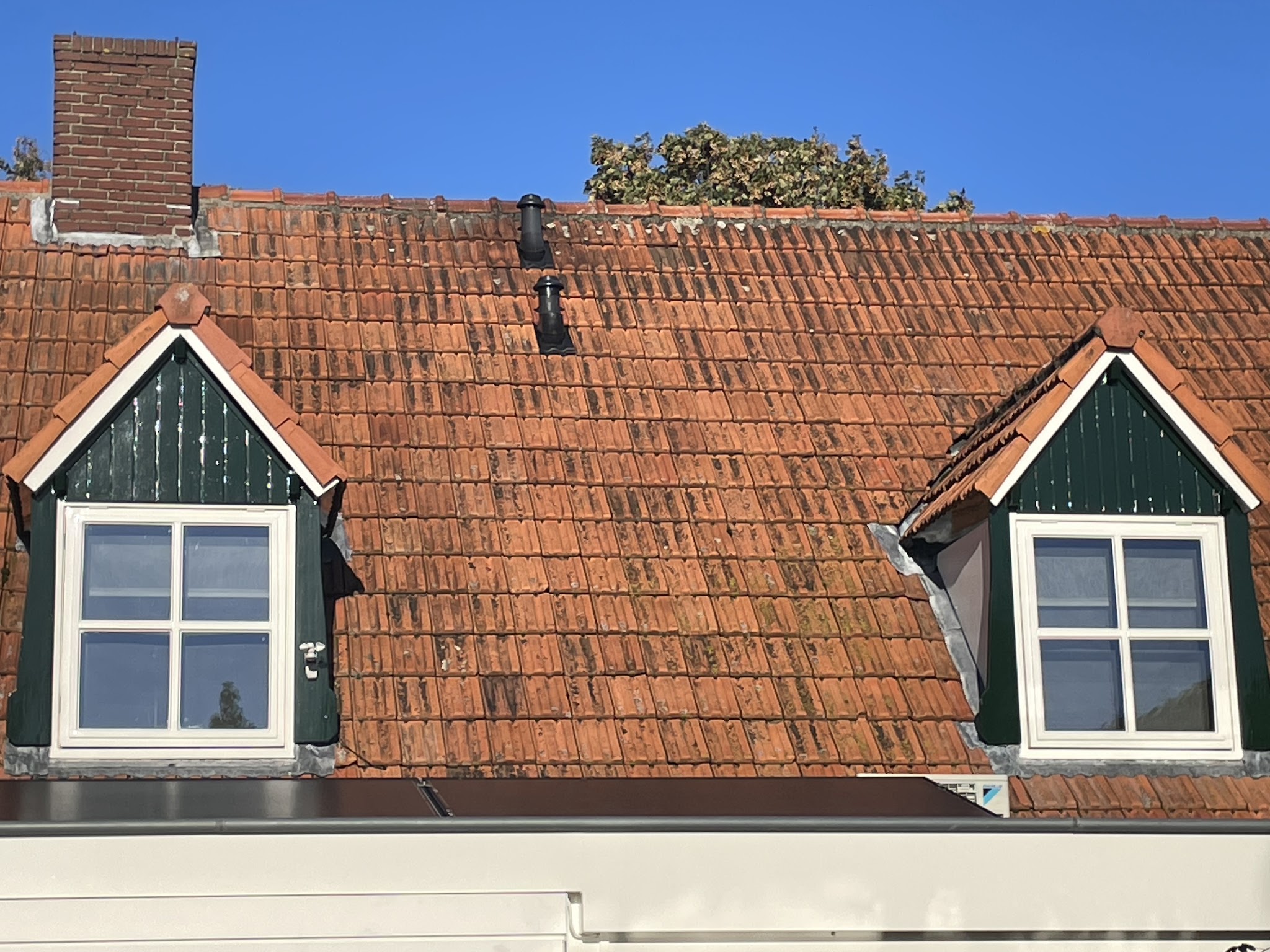 Twee dakkapellen met donkergroene betimmering en crèmekleurige kozijnen op een oranje pannendak