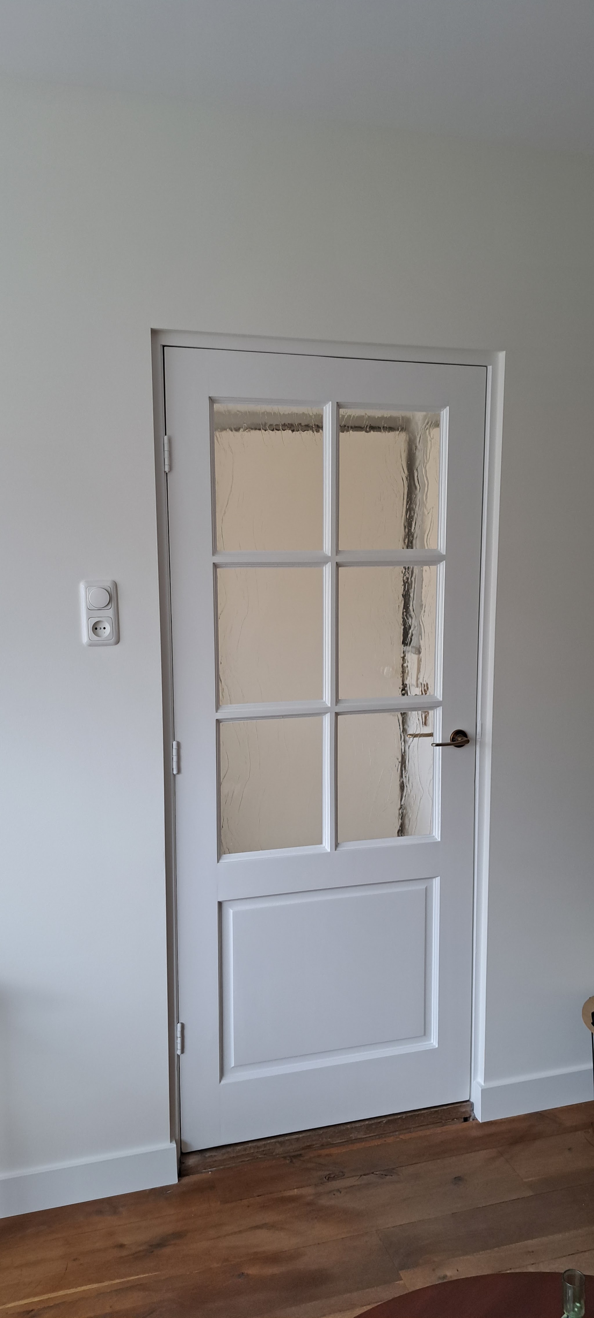 Wit geschilderde paneeldeur met glas in een lichte gang