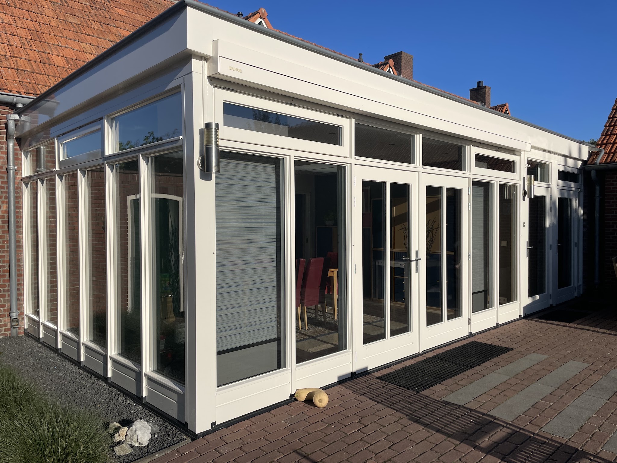 Serre met wit geschilderde kozijnen en deuren aan een terras met klinkers