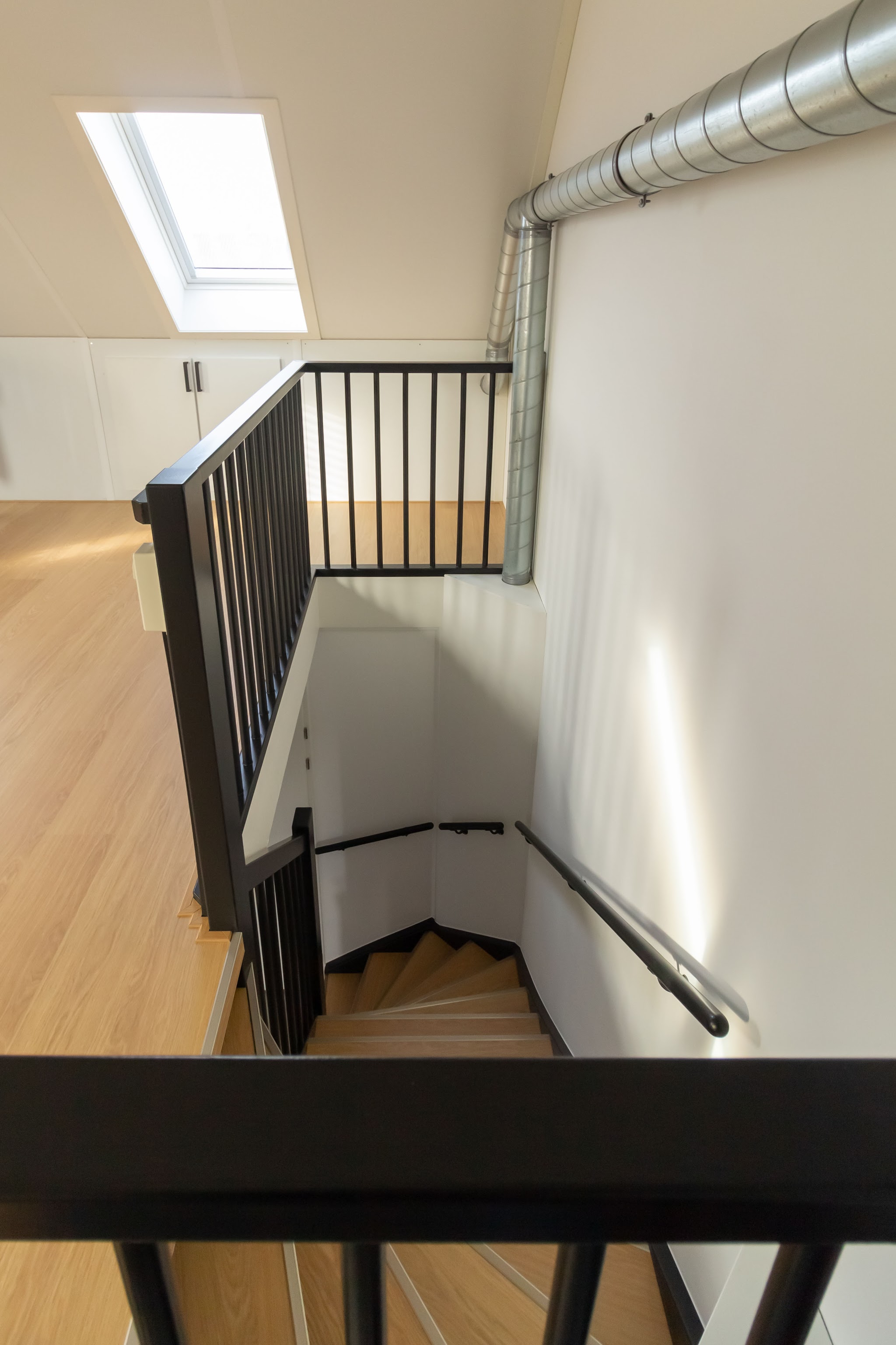 Trapgat van bovenaf met zwarte balustrade en daklicht